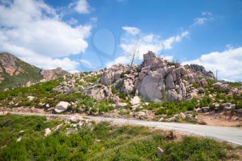 Landscape of South Corsica with mountain road and rocks under cloudy sky