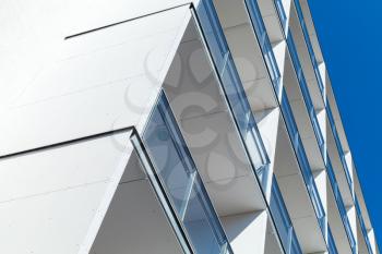 Abstract fragment of modern architecture, white walls and glass of balconies under blue sky
