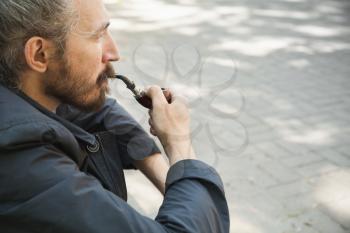 Bearded man smoking pipe, outdoor portrait with selective focus