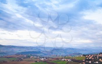 Rural panorama of Italian countryside. Province of Fermo, Italy. Village on a hill under dramatic blue cloudy sky