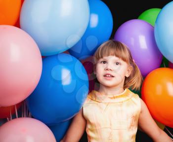 Studio portrait of Caucasian blond little girl with colorful balloons on black