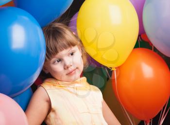 Studio portrait of funny little Caucasian blond girl with colorful balloons over back background
