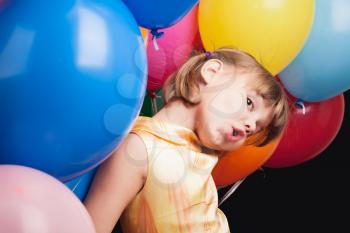 Studio portrait of funny little Caucasian blond girl with colorful balloons over back wall