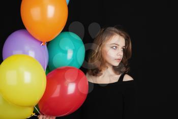 Close up studio portrait of beautiful teenage blond girl with colorful balloons over black background