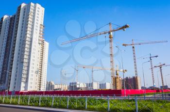 Block of flats under construction, working cranes are under blue sky