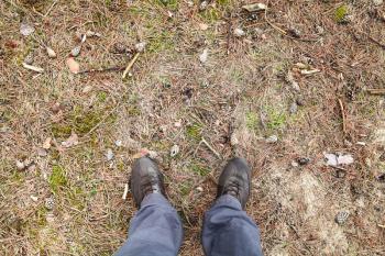 Male feet in brown shoes standing on dirty forest ground, first person view 