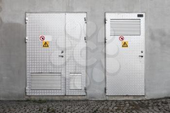 Metal doors with High Voltage warning signs in gray concrete industrial wall, background photo texture, front view