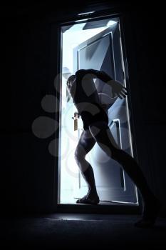Man enters opening door from black room and looks inside to the light, blue toned photo