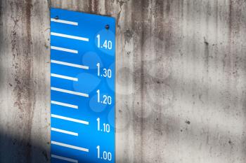 Blue tide level measurement scale on concrete mooring wall in port