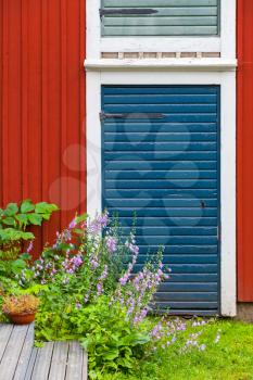 Porvoo, Finland. Old traditional Finnish architecture fragment. Decorative flowers near red blue closed door in red wooden wall