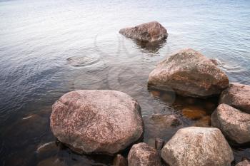 Coastal red granite stones lay in still lake water