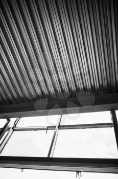 Generic industrial building is under construction. Interior fragment with shining corrugated metal ceiling and empty windows, vertical black and white photo