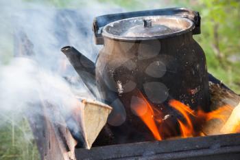 Old used black boiling teapot on bonfire