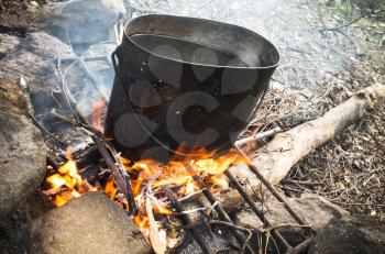 Old sooty black pan with boiling water stands on a bonfire