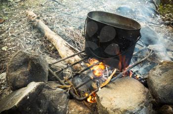 Old used black pan with boiling water stands on a bonfire