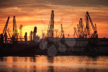 Silhouettes of cranes and industrial cargo ships in port of Varna at sunset