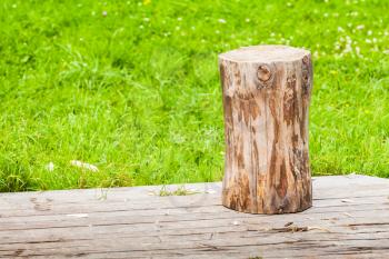 Log stands on rural wooden flooring in summer garden with fresh green grass on a background