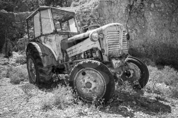 Old abandoned rusted tractor stands on dry grass. Black and white photo