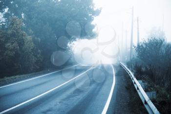 Empty rural highway in autumn foggy morning, stylized photo with cold blue tonal correction filter effect
