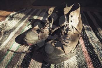 Old sneakers stand on striped knitted carpet. Retro stylized photo with tonal correction filter effect, old style