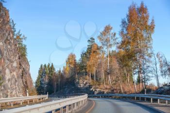 Turning rural Norwegian road goes near rocks in autumn season