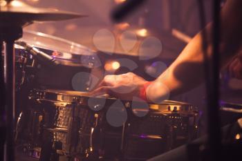 Vintage warm toned live music background, drummer plays with drumsticks on rock drum set. Closeup photo with soft selective focus