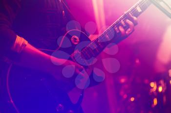 Electric guitar player on a stage with colorful blue and purple scenic illumination, soft selective focus