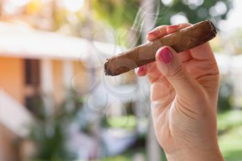 Handmade cigar in female hand, close-up outdoor photo with selective focus