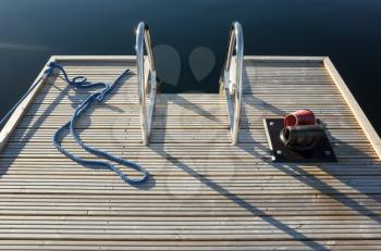 Small floating wooden marina pier with ropes and metal railings