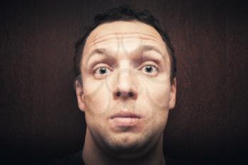 Young surprised Caucasian man. Close-up studio face portrait over dark wooden wall background, selective focus