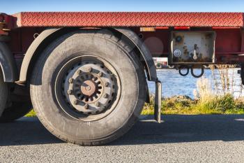 Fragment of cargo truck, red trailer wheel on asphalt road