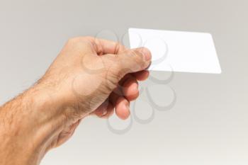 Male hand with white empty card over gray wall background, closeup photo with selective focus