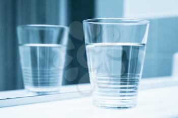 Glass of water stand on shelf near mirror, blue toned closeup photo