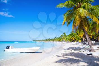 Coconut palms and white pleasure boat are on white sandy beach of Saona island. Caribbean Sea coast, Dominican republic