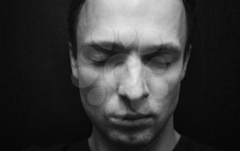 Young Caucasian man with closed eyes. Studio portrait over dark wall background, black and white photo
