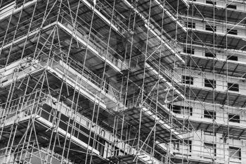 Modern living house is under construction, block of flats facade fragment with scaffolding structures, black and white photo