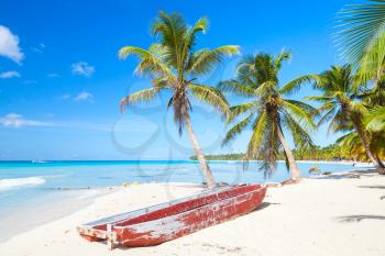 Coconut palms and old red pleasure boat are on white sandy beach. Caribbean Sea, Dominican republic, Saona island coast, touristic resort