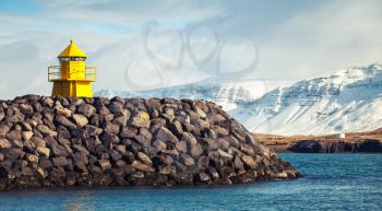 Yellow lighthouse tower on stone breakwater, entrance to Reykjavik cargo port. Vintage toned photo, retro photo filter effect