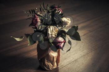 Bouquet of dried red and white roses stands on wooden table, closeup low key photo with soft selective focus, retro stylized tonal correction effect