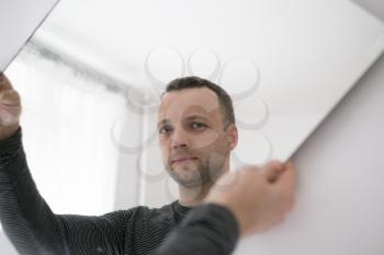 Portrait of young adult European man standing near white wall with mirror