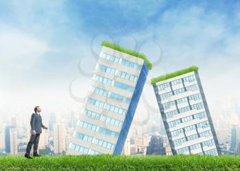 Businessman looks at two falled buildings standing on the grass