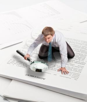 Man with big loupe sits on papers leaning on his palm and reading an agreement