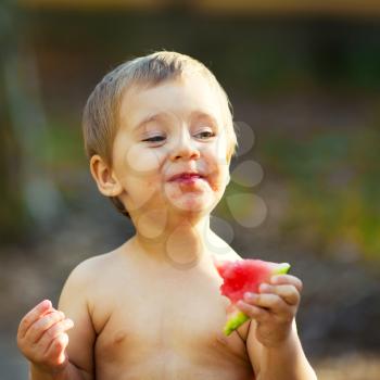 Happy child eating watermelon outdoors in summer