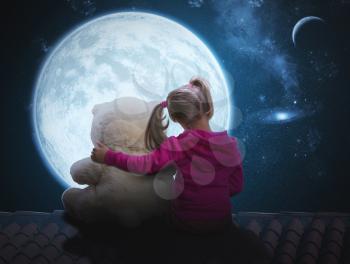 Small cute girl sitting with toy bear on the roof and looking at the moon