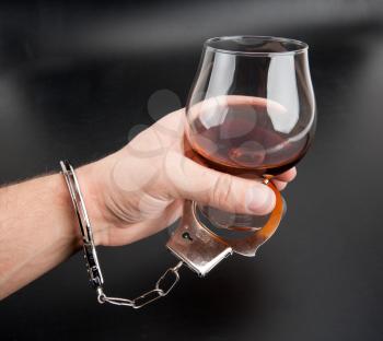 A hand locked to glass of alcohol by handcuffs