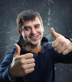 Young man giving thumb up against grungy wall