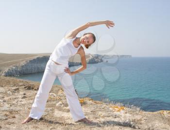 Beautiful woman in white practices Yoga in mountains against the sea