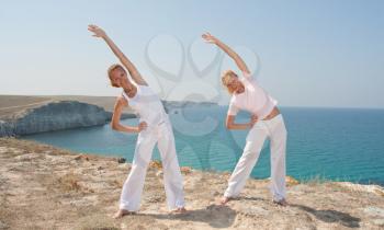 Women in white cloth practices Yoga in mountains against the sea
