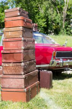 Huge heap of old suitcases standing on the grass near a red car