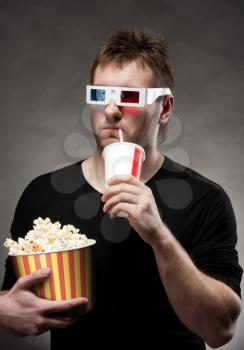 Portrait of man watching 3D movie, drinking cola and holding bucket of popcorn